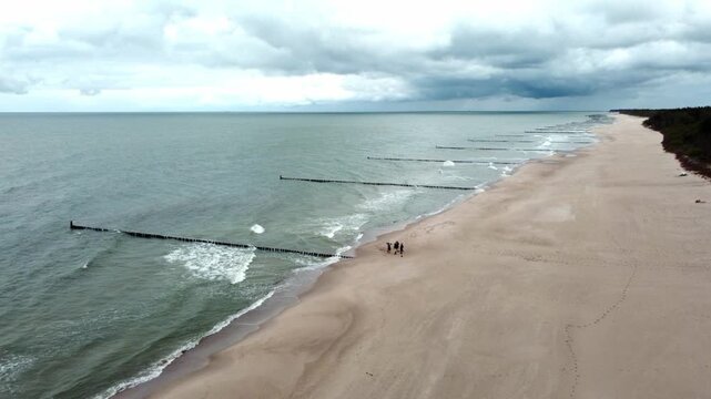 Drone slowly pulls back and ascends above a wide sandy beach with tourists along the Hel Peninsula coast in Poland.