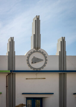 White Art Deco facade decorated with a gear and locomotive emblem above a doorway, Namibe Province, Namibe, Angola