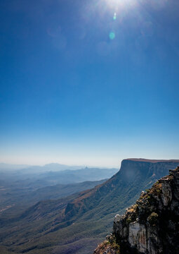 Panoramic view over the layered mountains and cliff edge of the Serra da Chela escarpment with sun flare in the sky, Huila Province, Humpata, Angola