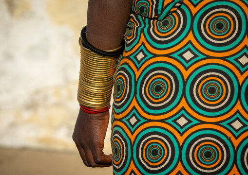 Close-up of a Mwila woman's forearm stacked with brass rings beside a circle-patterned dress, Huila Province, Lubango, Angola
