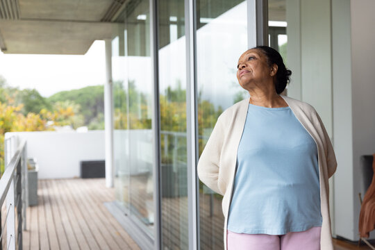 Senior African American woman standing on deck in cardigan pink pants near glass doors, copy space