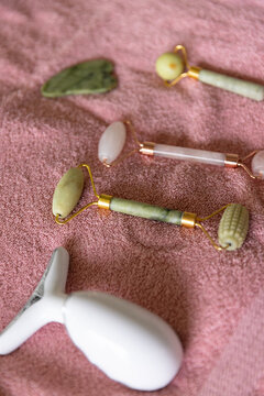Green jade roller resting on plush pink towel, with rose quartz roller and white T-shaped massager