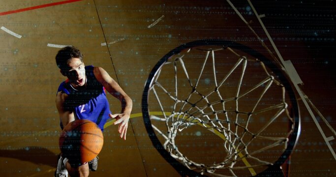 Leaping adult player driving to hoop on hardwood court, in blue jersey holding basketball near rim