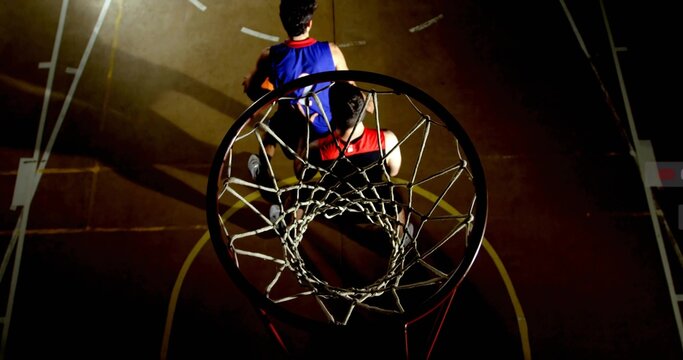 Framing basketball rim and net casting shadow on court, with red and blue jerseys
