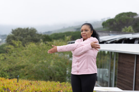 Senior African-American woman stretching on deck by glass rail in pink coat and leggings