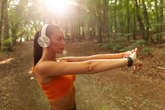 Young athletic woman stretching her arms before outdoor training on forest path