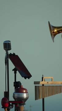 Brass cornet performer plays music outdoors against clear sky near a vintage microphone. Static medium shot.
