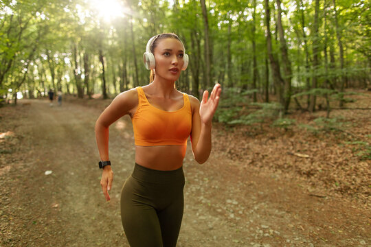 Young woman jogging through forest trail during outdoor fitness session, wearing headphones
