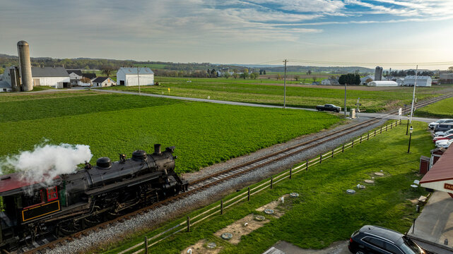 Steam Train Travels Along Tracks Near Farmland in Rural Area During Bright Day