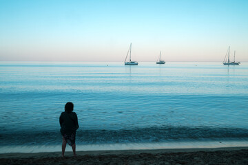 El Playazo Rodalquilar Sunset. Woman observes tranquil sea and sailboats. © Ana