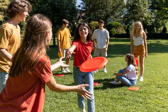 Group of happy young friends playing with flying discs on a sunny green lawn in park