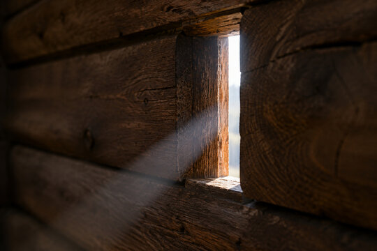 Close-up of a narrow arrow slit in a wooden wall, a single beam of light shining through, detailed wood.