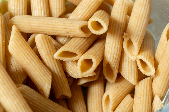 Close up of uncooked whole wheat penne pasta showing tubular shapes and ridged texture. Natural dry Italian pasta background and healthy food ingredient concept.