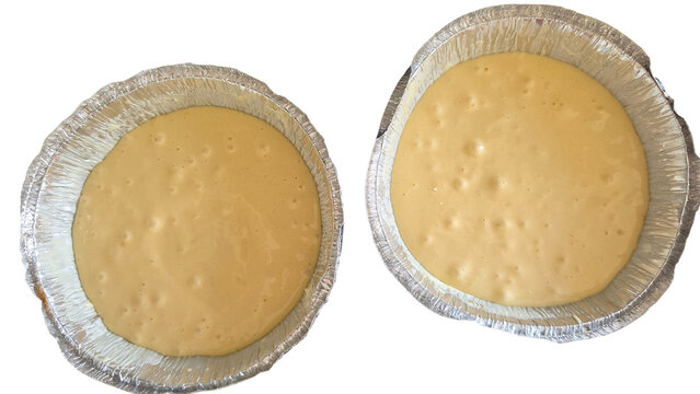 Two round aluminum foil baking pans filled with liquid cake batter on a transparent background