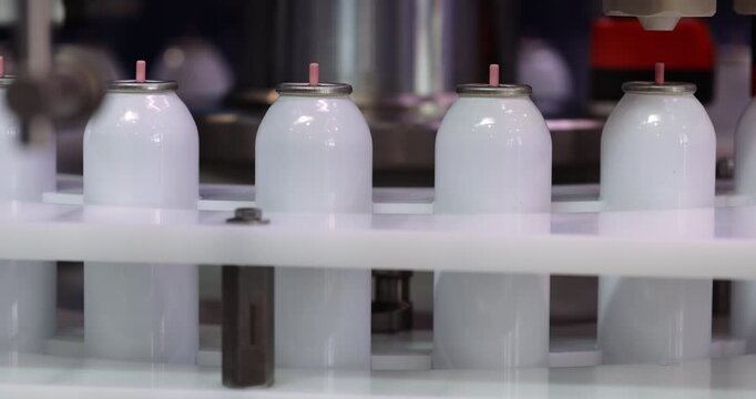 Hair lacquer blank bottles filled by automated machinery closeup. Opaque flasks for hairstyling cosmetic products manufacturing with modern factory machines