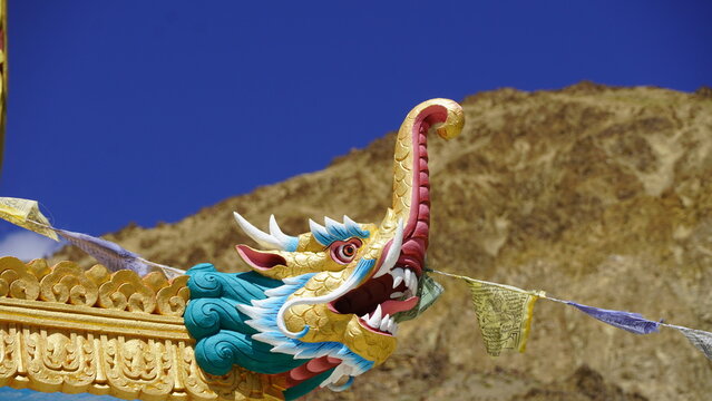 Colorful dragon statue with prayer flags against clear blue sky in golden Ladakh mountains, India, vibrant autumn hues, sunny day, panoramic view