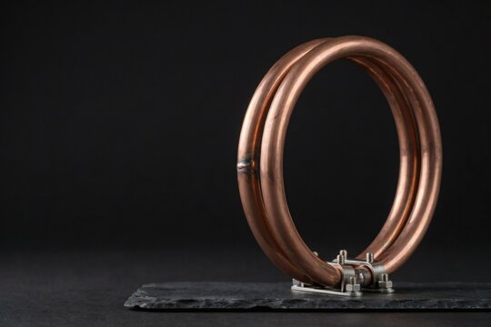 Copper coil standing on a slate slab against a deep black studio background