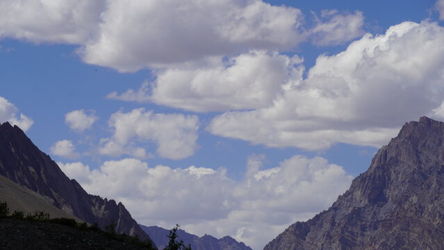 Rugged mountain peaks under partly cloudy sky with patches of blue in Ladakh, India; rocky terrain foreground; dramatic alpine landscape; summer day; high-altitude scenery; scenic view from valley