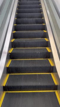 Escalator moving downward with black steps and yellow safety edges in a modern public facility, vertical video.