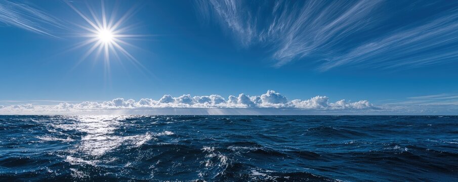 Bright sun shines over choppy blue ocean under a vast sky with clouds