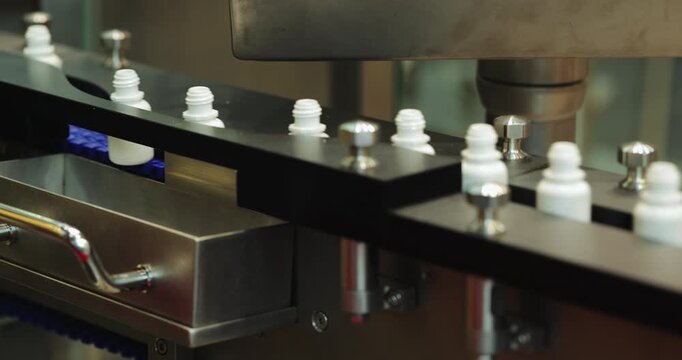 Automated station guides white medicine bottles with processing heads. Precision conveyor positions each container for controlled pharmaceutical operation