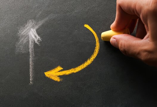 Hand draws curved arrow on chalkboard with chalk for direction