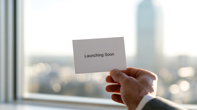 Business person hand hold white card with launching soon text message against office window background with bright city view during work day