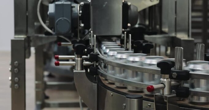 Empty metal cans move around curved conveyor inside automated brewery plant. Precision guides maintain alignment supporting continuous container transport