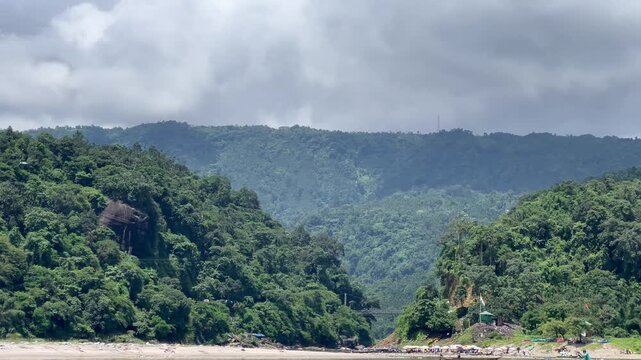 Jaflong Sylhet Local wooden boat crossing wide river against lush green mountains and cloudy sky backdrop