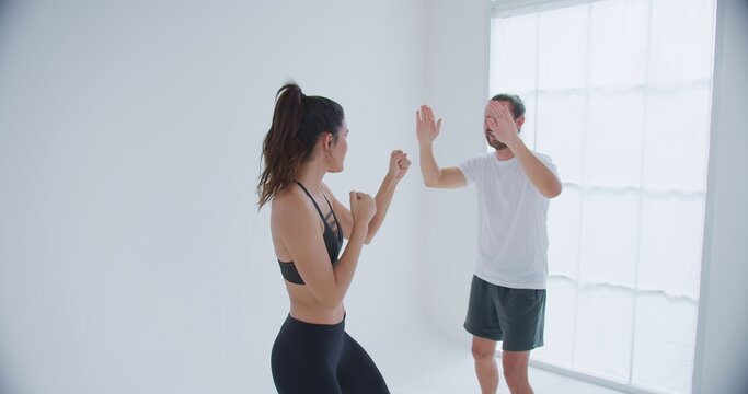 A personal trainer coaches a determined woman on boxing techniques, guiding her stance and form during a private lesson in a bright minimalist fitness studio.