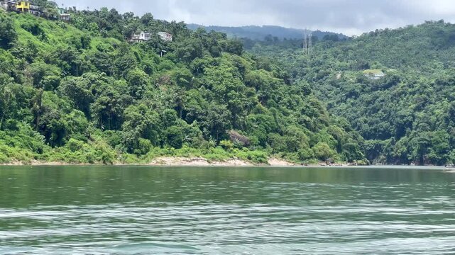 Jaflong Sylhet Scenic river cruise passing lush green forested hills and distant houses on cloudy day