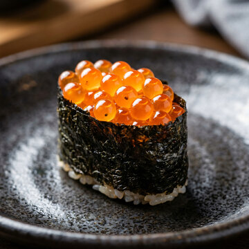 Fresh salmon roe sushi gunkan served on a dark textured ceramic plate.