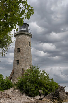 The iconic stone lighthouse on Pelee Island, Ontario, set against a dramatic cloudy sky, surrounded by lush greenery and rocky terrain.