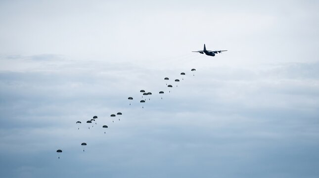 Military transport plane drops paratroopers in formation against cloudy sky