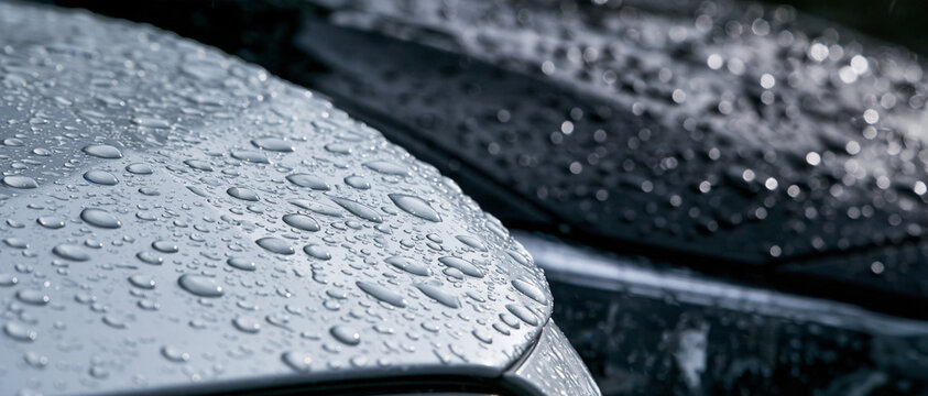 Close-up of sparkling water droplets on a sleek, silver metallic car surface after a fresh rainfall, showcasing the car's wax coating and water repellency with a softly blurred background