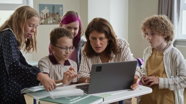 Caucasian middle aged teacher and school children studying on laptop during classroom lesson. Ideal for edtech advertising, modern school education campaigns and elearning video projects
