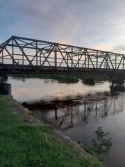 Fototapeta premium Old iron bridge over a rural river at sunset 