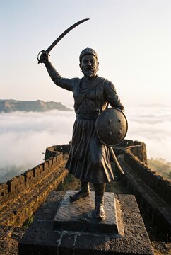 Bronze statue of Chhatrapati Shivaji Maharaj raising a sword on a hill fort rampart above a sea of morning clouds
