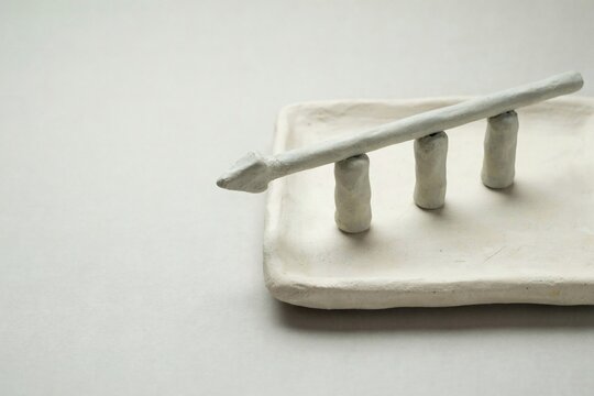 Pale clay arrow bar balanced on three small pillars on a handmade tray