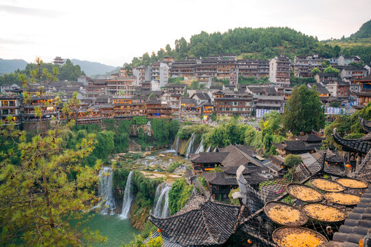 Panoramic view of Furong Ancient Town in China featuring traditional buildings a waterfall and crops