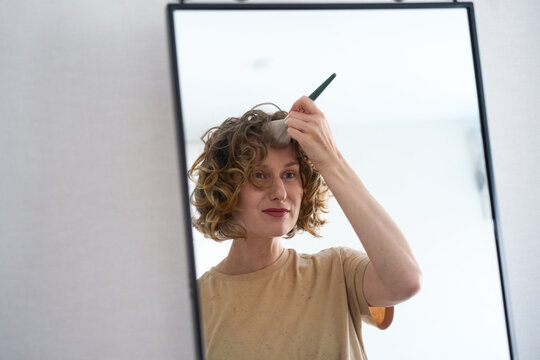 Woman applying powder with a brush in a mirror.