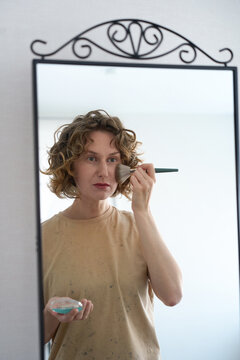 Woman applying powder with a brush in a mirror.