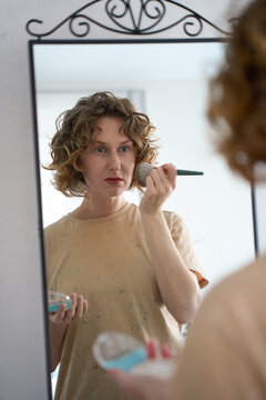 Woman applying powder with a brush in a mirror.
