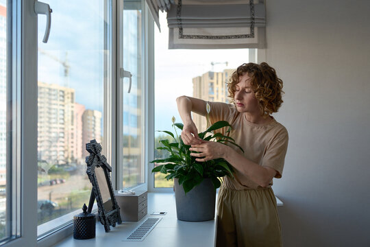 Woman holding a potted peace lily by the windowsill.