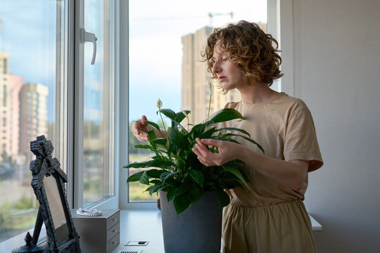 Woman holding a potted peace lily by the windowsill.