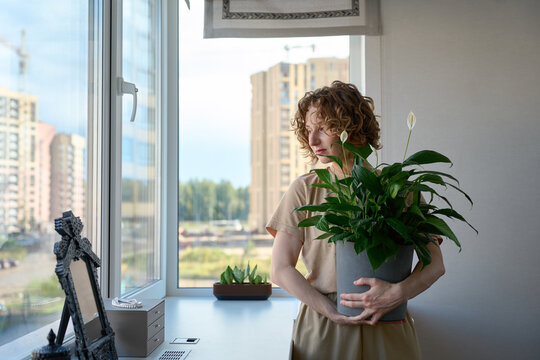 Woman holding a potted peace lily by the windowsill.