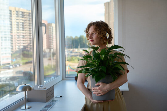 Woman holding a potted peace lily by the windowsill.
