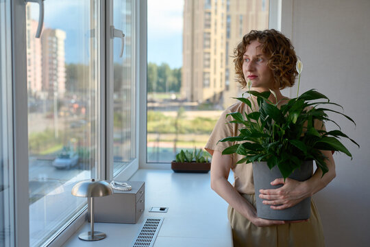 Woman holding a potted peace lily by the windowsill.