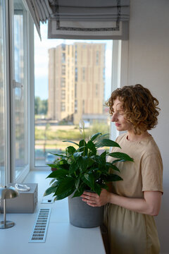 Woman holding a potted peace lily by the windowsill.