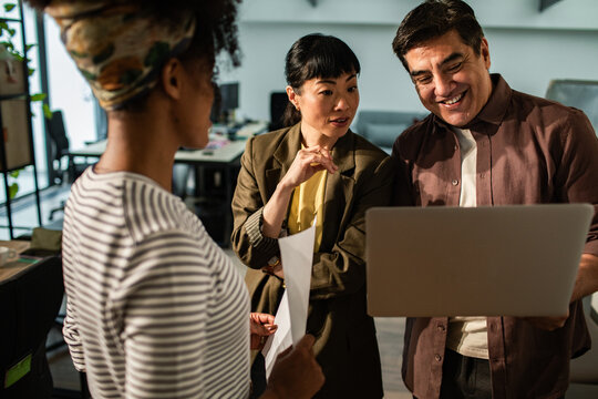 Diverse coworkers collaborating on laptop in modern office